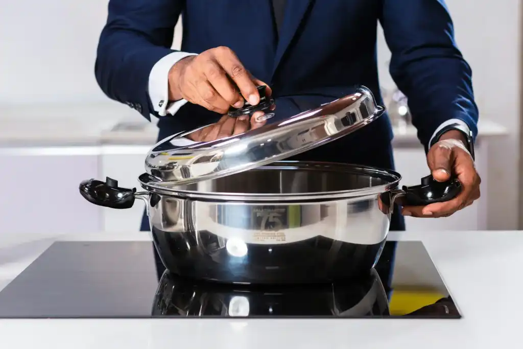 Person lifting the lid of a stainless steel pot on a sleek black induction cooktop