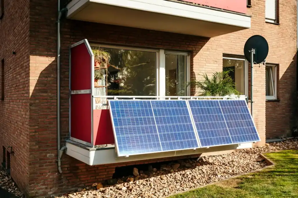 Two plug-in solar panels mounted on the railing of a ground-floor apartment balcony in the sun